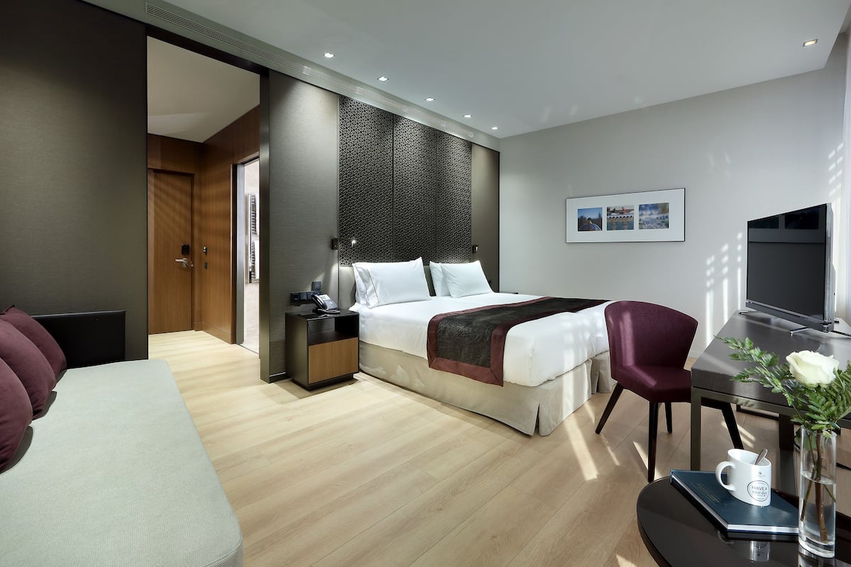 Una habitación de hotel moderna con cama, mesita de noche, silla, escritorio y televisor.