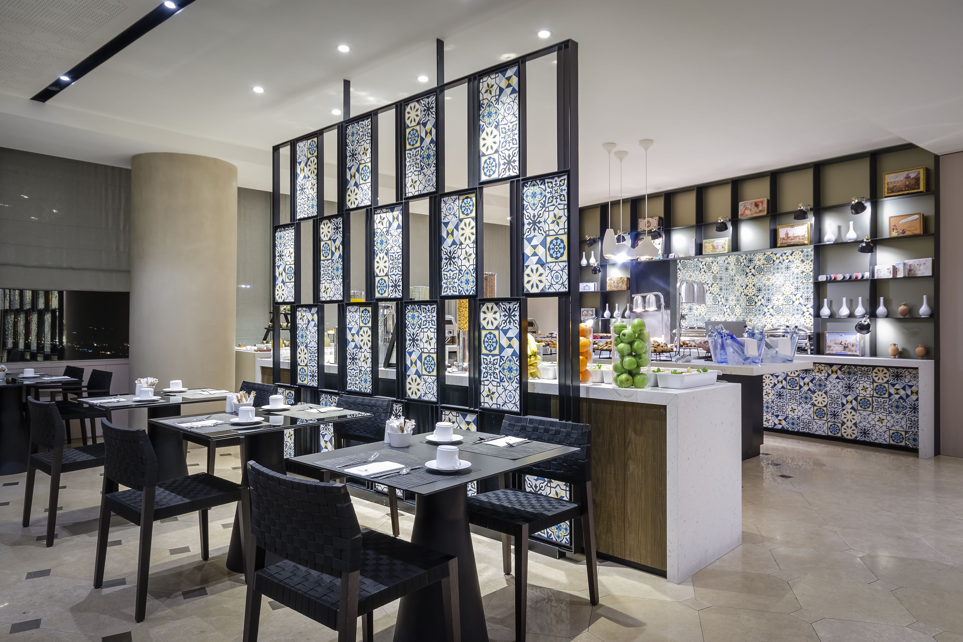 Ein modernes Restaurant mit schwarzen Stühlen, weißen Tischen und einer dekorativen Trennwand mit blau-weißen Fliesen.