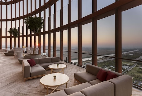 A spacious lounge area with a curved wooden ceiling, large windows offering a view of a river and cityscape, and comfortable seating arrangements.