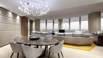 A modern living room with a round dining table, grey upholstered sofas, and a large window offering a city view.