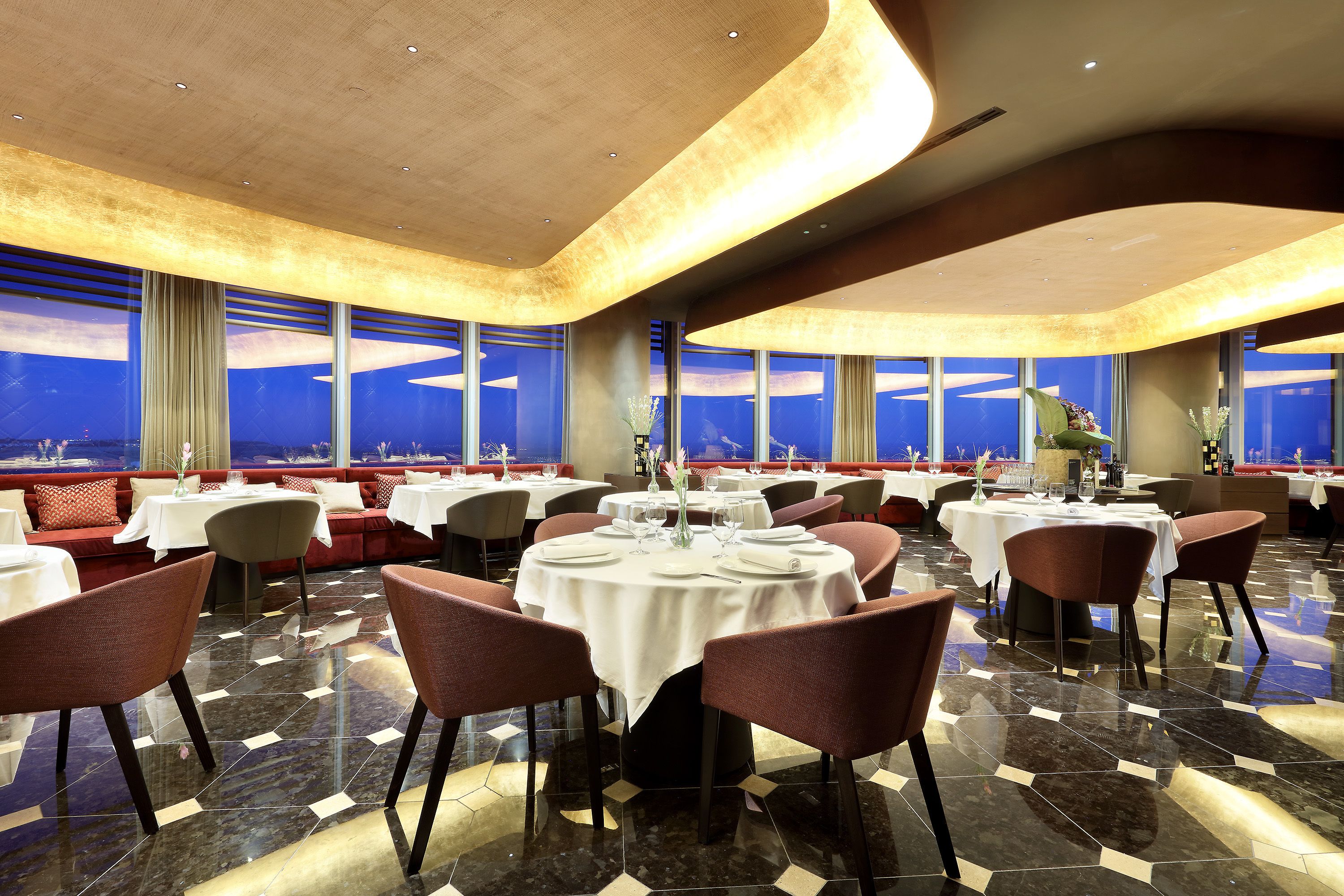 Un restaurant avec des tables et des chaises rondes, de grandes fenêtres offrant une belle vue et un sol ciré.