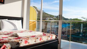 Un dormitorio con una cama grande, una ventana con vistas a una colina y un balcón con barandillas de vidrio.