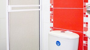 Inodoro blanco con un adhesivo azul, puerta de ducha y paredes con azulejos rojos y blancos.