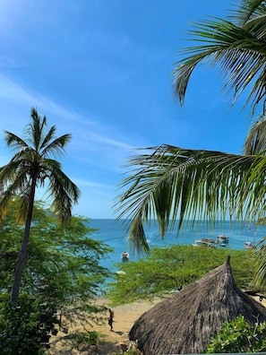 Una playa con palmeras, una cabaña de techo de paja y barcos en el agua.