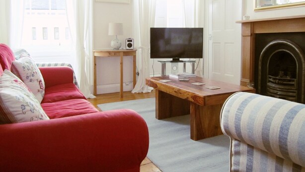 A living room with a red sofa, a wooden coffee table, a television, and a fireplace. - Edinburgh City Retreat Apartments (Edinburgh)