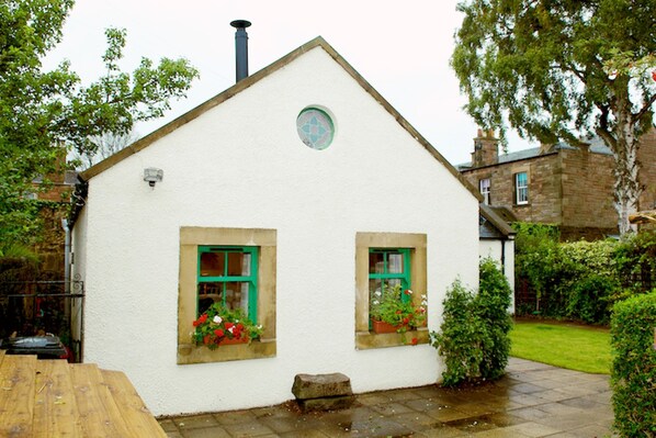 A white building with two windows, each with green shutters and flower boxes.