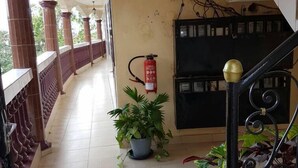A covered corridor with tiled flooring, a fire extinguisher, a potted plant, and a staircase with ornate railings. - Bs VIP Appartement (Yaoundé)