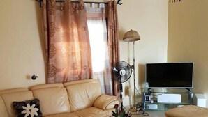 A living room with a beige sofa, a glass coffee table, a TV, and a floor lamp. - Bs VIP Appartement (Yaoundé)