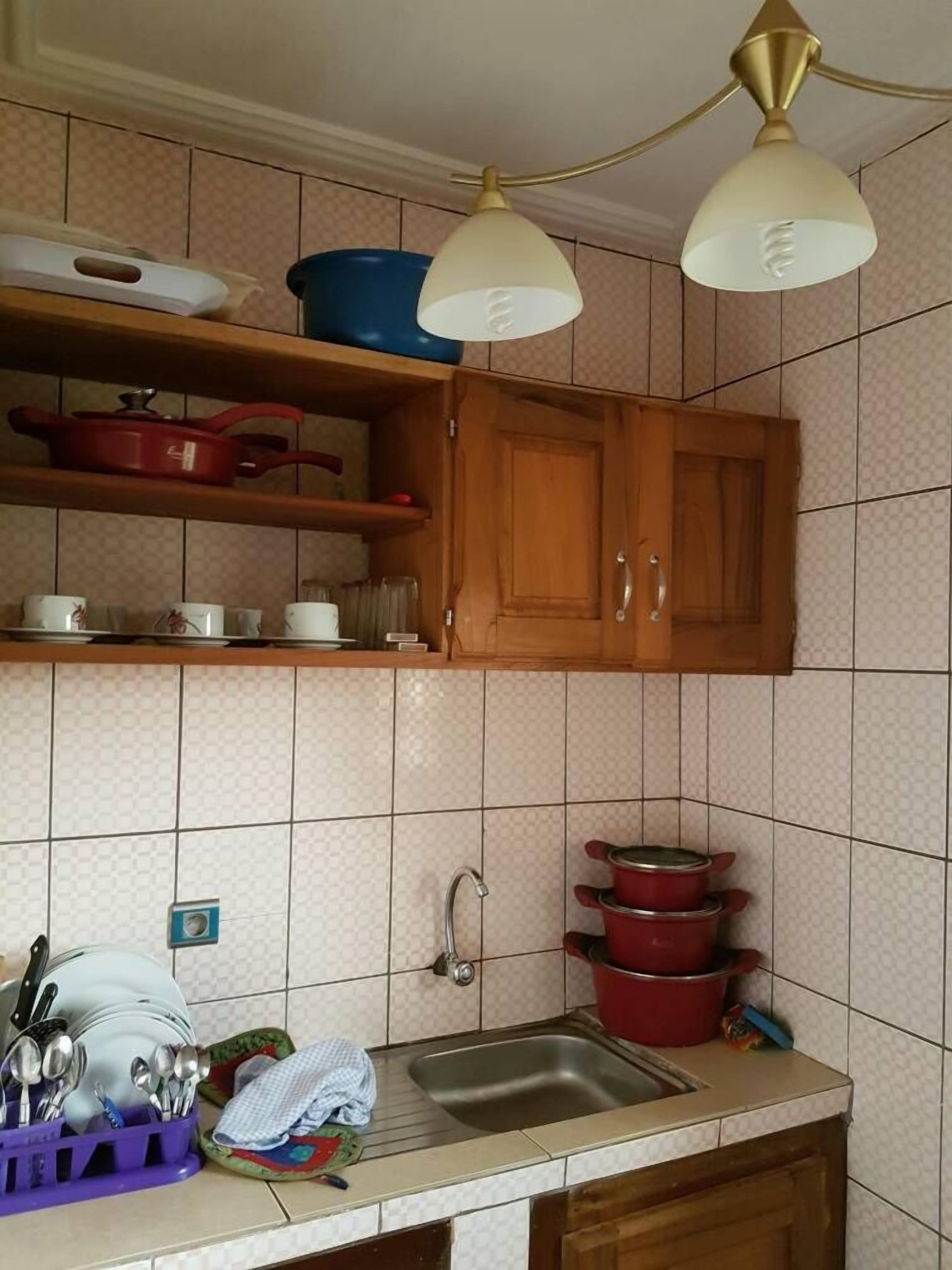 Une cuisine avec des meubles de rangement en bois, un évier et un plan de travail sur lequel sont disposés divers ustensiles de cuisine.