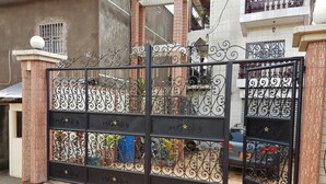 A black metal gate with decorative patterns and a number plate. - Bs VIP Appartement (Yaoundé)