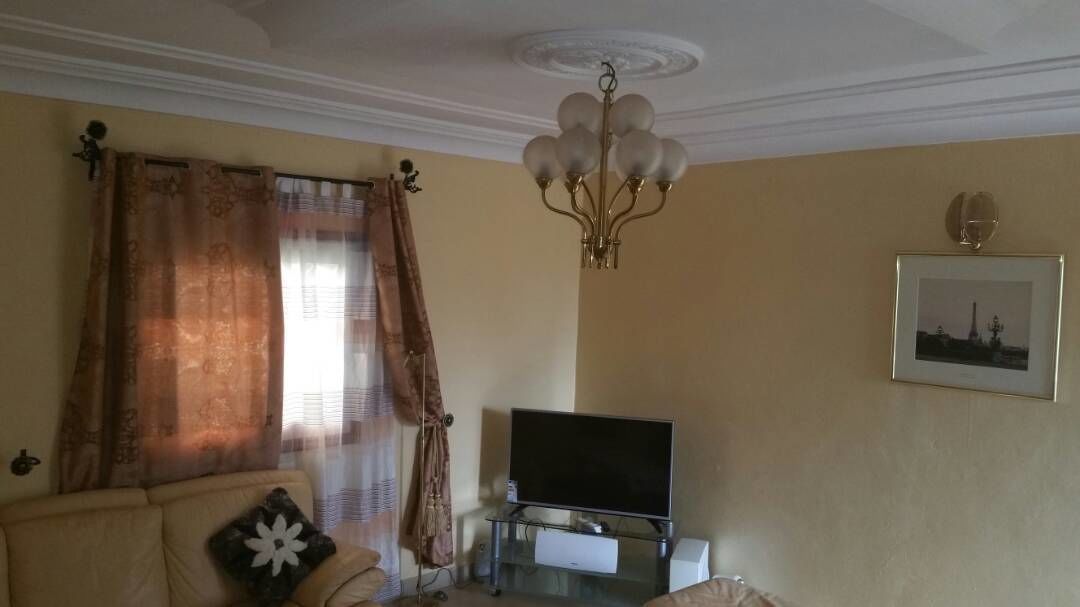 Un salon comprenant un canapé, une table basse en verre, un téléviseur, un lustre et un tableau encadré accroché au mur.