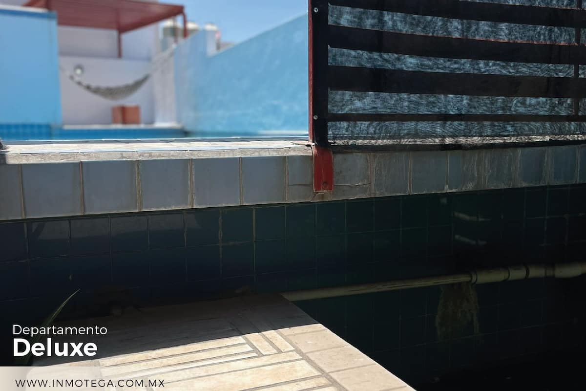 A poolside area with a tiled deck, a hammock, and a view of a building with a red roof.