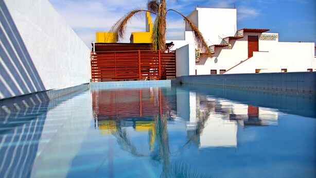 A swimming pool with clear water reflecting the surrounding buildings and palm tree.