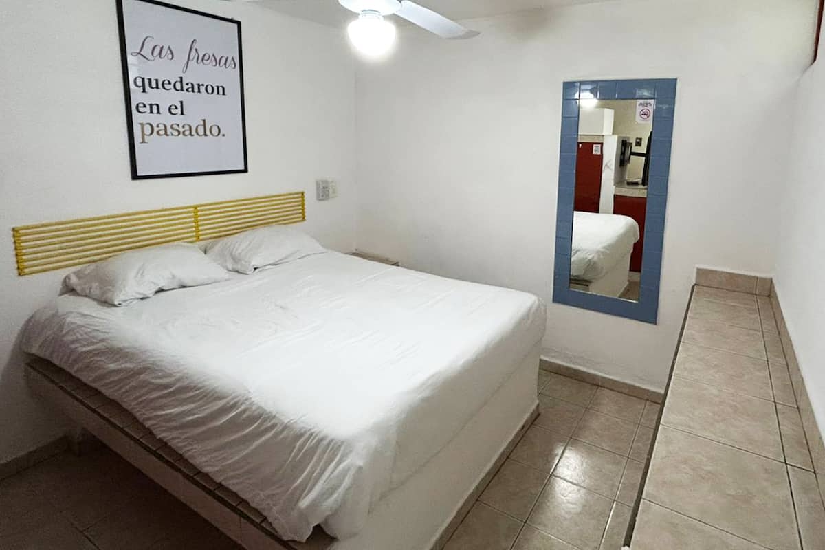 A bedroom with a bed, a ceiling fan, a wall-mounted mirror, and a framed quote on the wall.