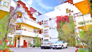 A multi-story hotel with balconies, a parking area, and signage indicating the building's name and location.