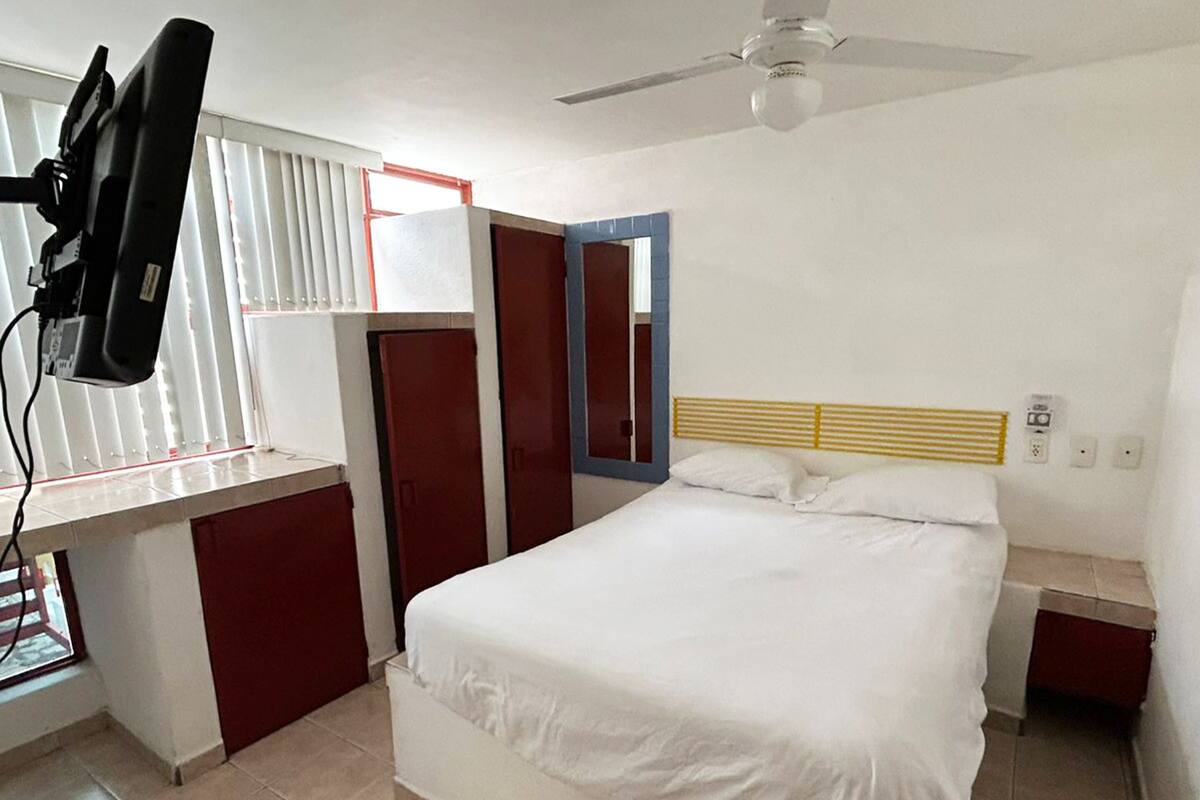 A bedroom with a bed, a desk, a ceiling fan, and a window with blinds.