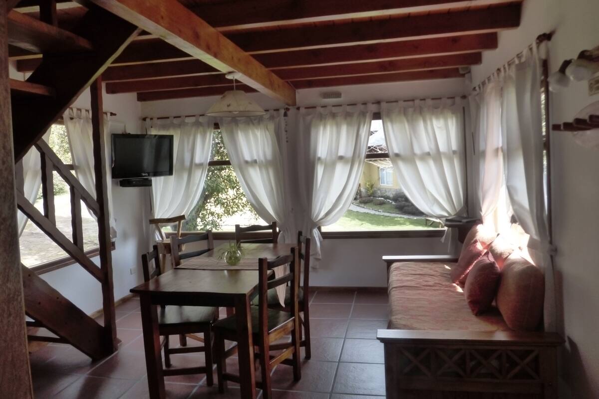 Une pièce chaleureuse avec un plafond en bois, une table à manger avec des chaises, un canapé et un téléviseur fixé au mur.