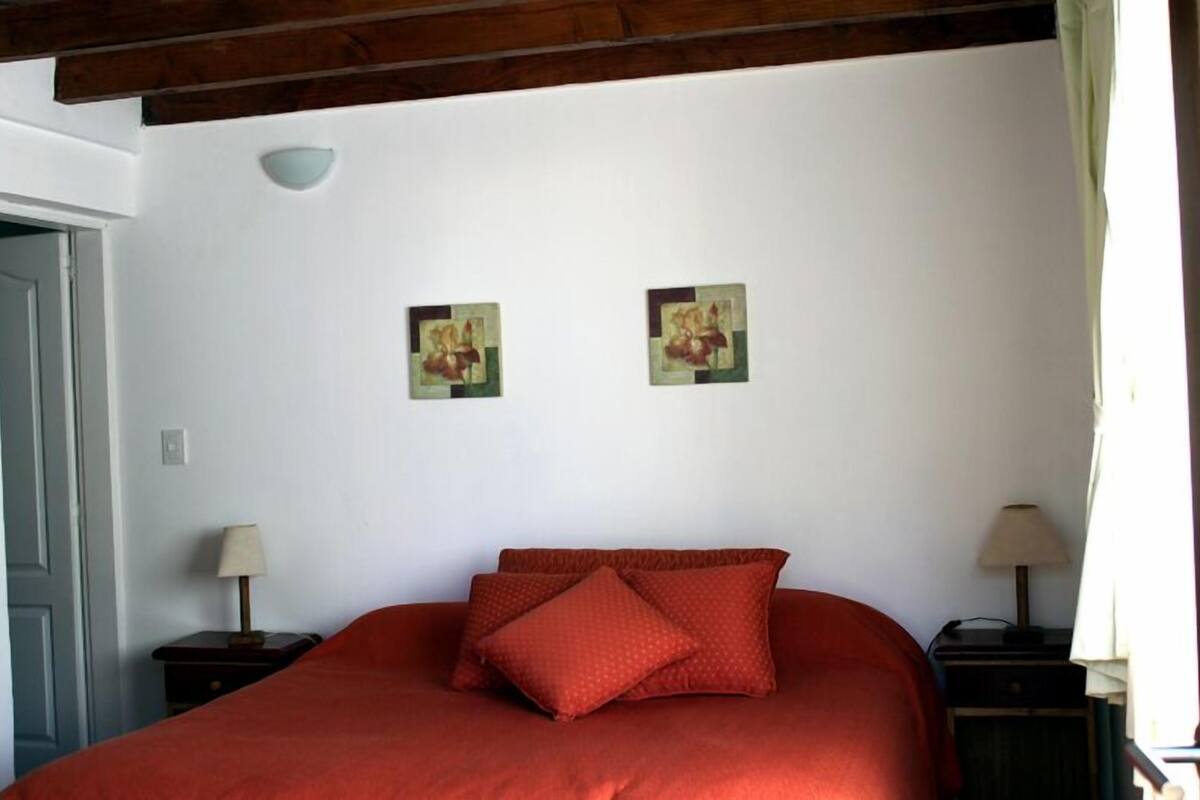 Une chambre à coucher avec un grand lit, deux petites tables de chevet avec des lampes et deux cadres photos fixés au mur.