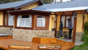 A wooden deck with built-in planters, a stone wall, and a house with a metal roof and wooden windows. - Tierra Sureña (San Carlos de Bariloche)