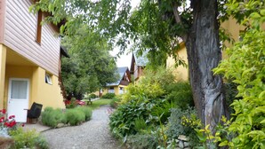 A pathway leading to a yellow building with a door and window, surrounded by lush greenery and a tree. - Tierra Sureña (San Carlos de Bariloche)