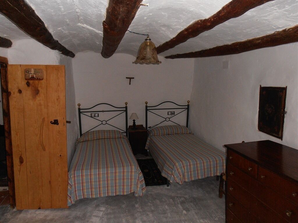 A room with two single beds, a wooden wardrobe, a door, and a ceiling with exposed beams.