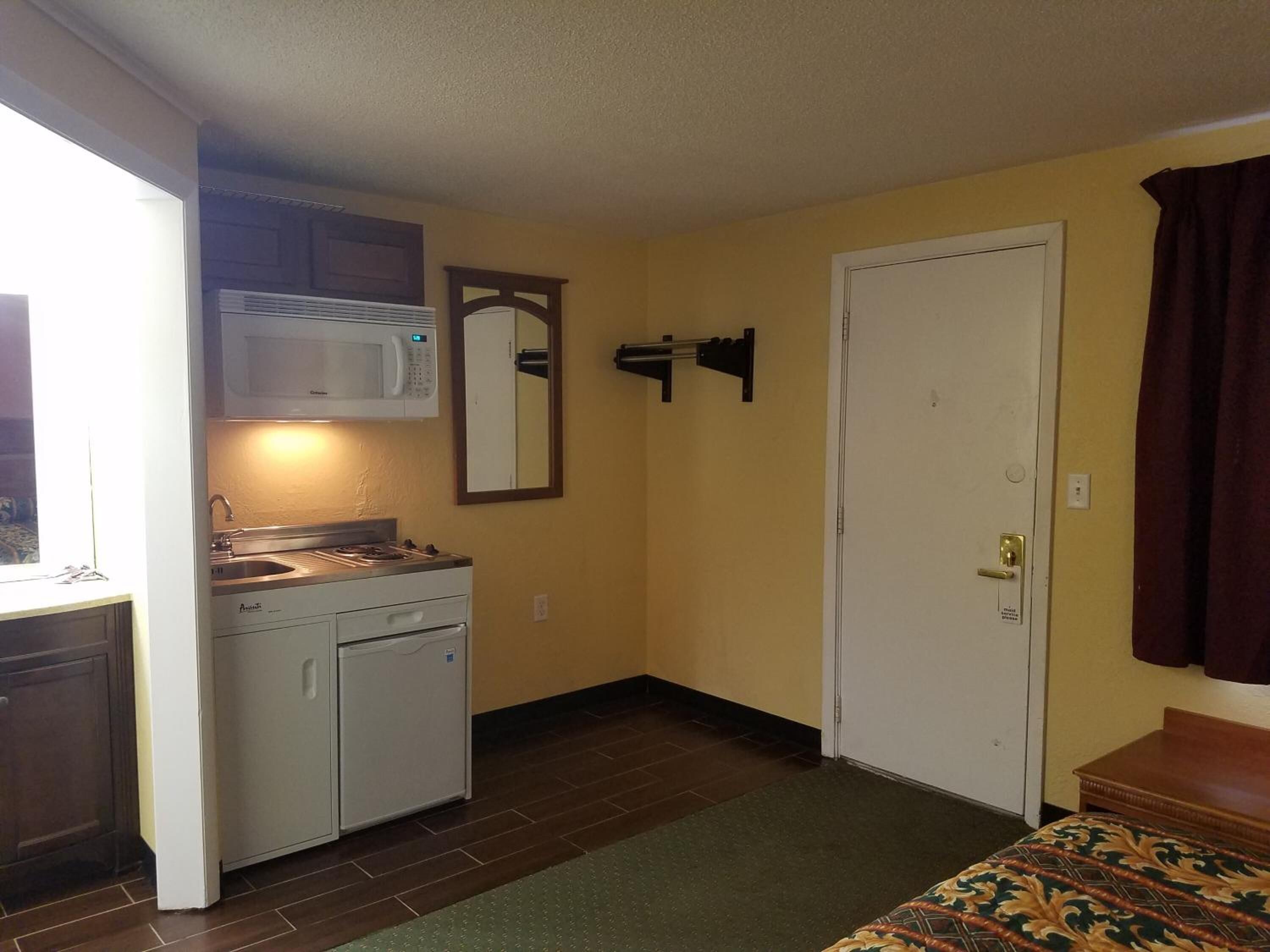 Una kitchenette compacta con microondas, estufa y pileta, una puerta con manija, y un edredón estampado.