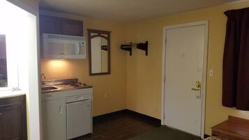 Una kitchenette compacta con microondas, estufa y pileta, una puerta con manija, y un edredón estampado.