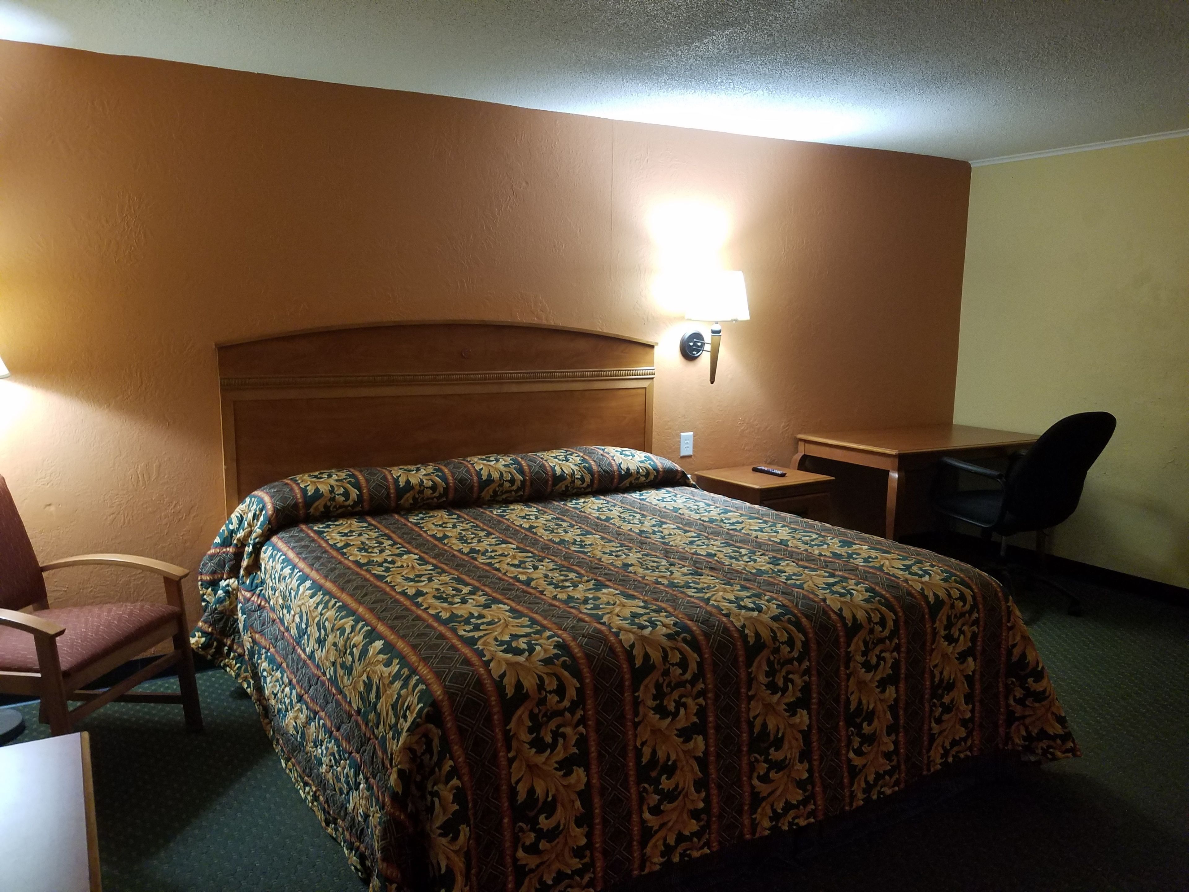 A hotel room with a large bed, a desk, a chair, and a nightstand.