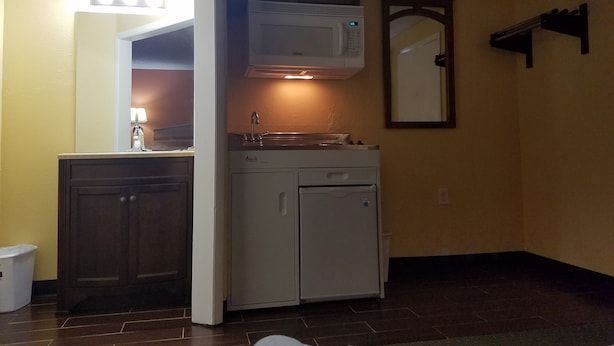 Cocina compacta con microondas, estufa y lavabo. Hay un mueble con un espejo sobre el lavabo y un estante pequeño sobre el microondas. La cocina tiene piso de baldosas y paredes amarillas.