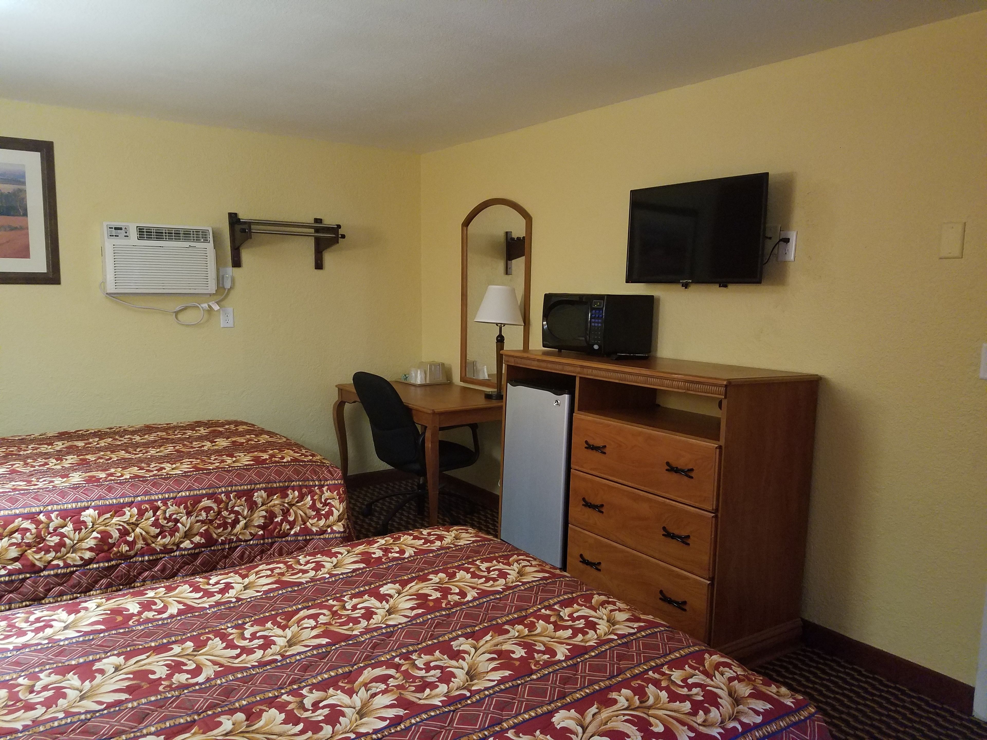 Habitación de hotel con dos camas, un escritorio con una silla, refrigerador, microondas, televisor y aire acondicionado instalado en la pared.