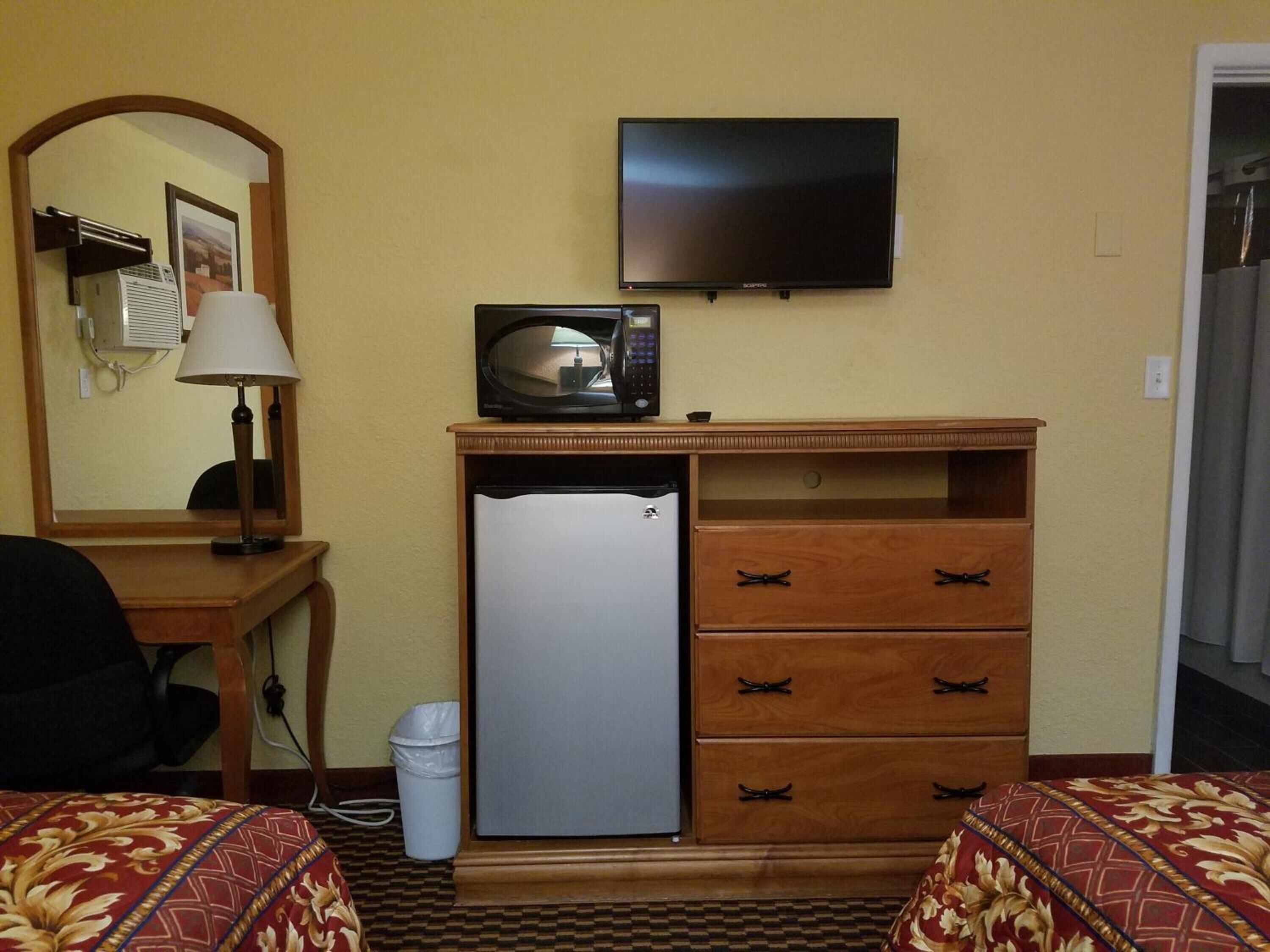 Une chambre d’hôtel équipée d’un lit, d’un bureau avec une lampe, d’un four à micro-ondes, d’un réfrigérateur et d’un téléviseur fixé au mur.