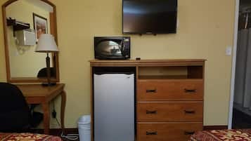 Une chambre d’hôtel équipée d’un lit, d’un bureau avec une lampe, d’un four à micro-ondes, d’un réfrigérateur et d’un téléviseur fixé au mur.