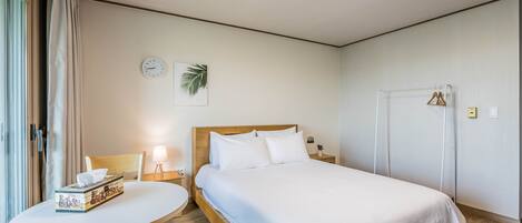 A hotel room with a bed, a table, and a chair. There is a clock and a plant on the wall.