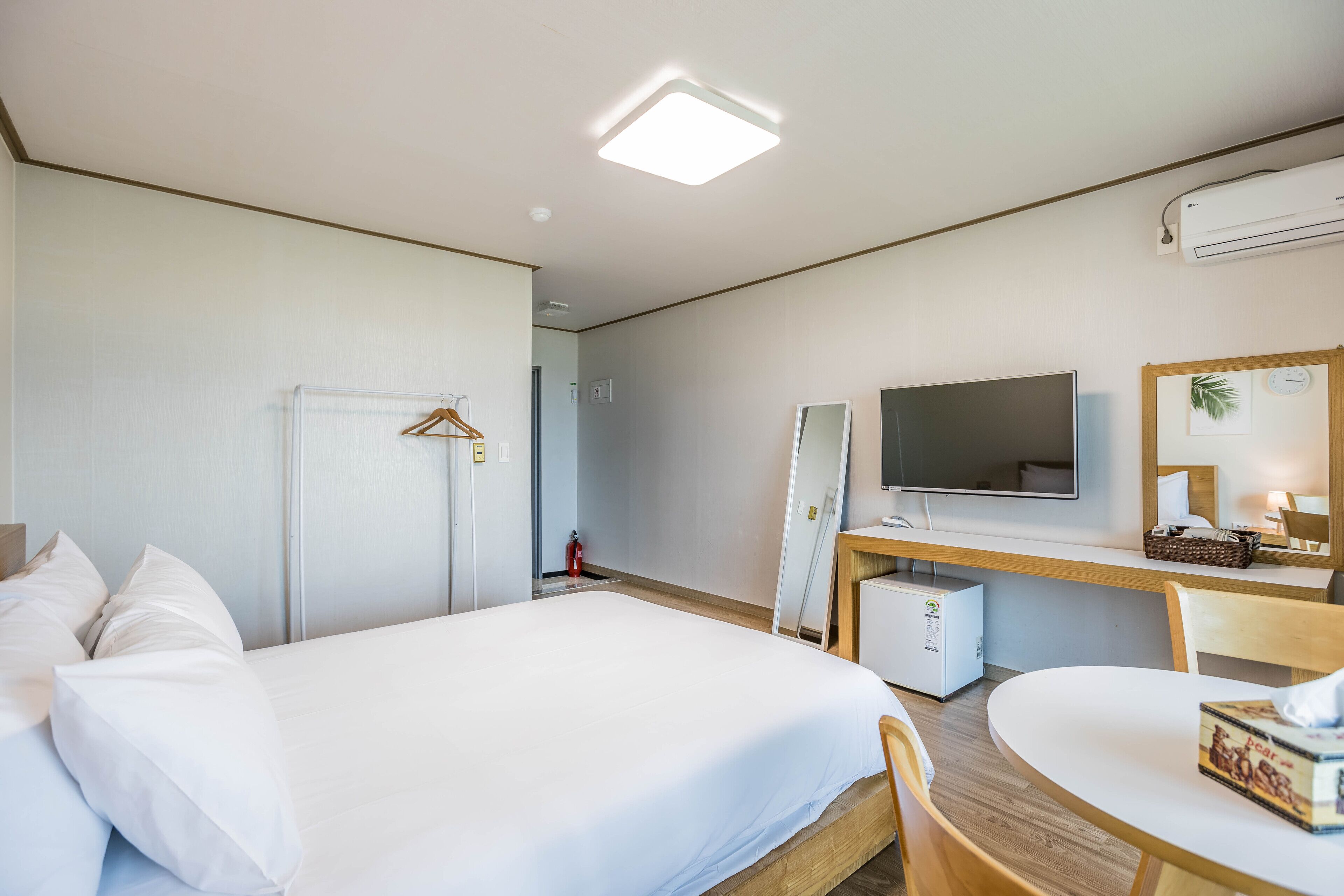Quarto de hotel com uma cama, uma escrivaninha com computador, televisão e espelho.