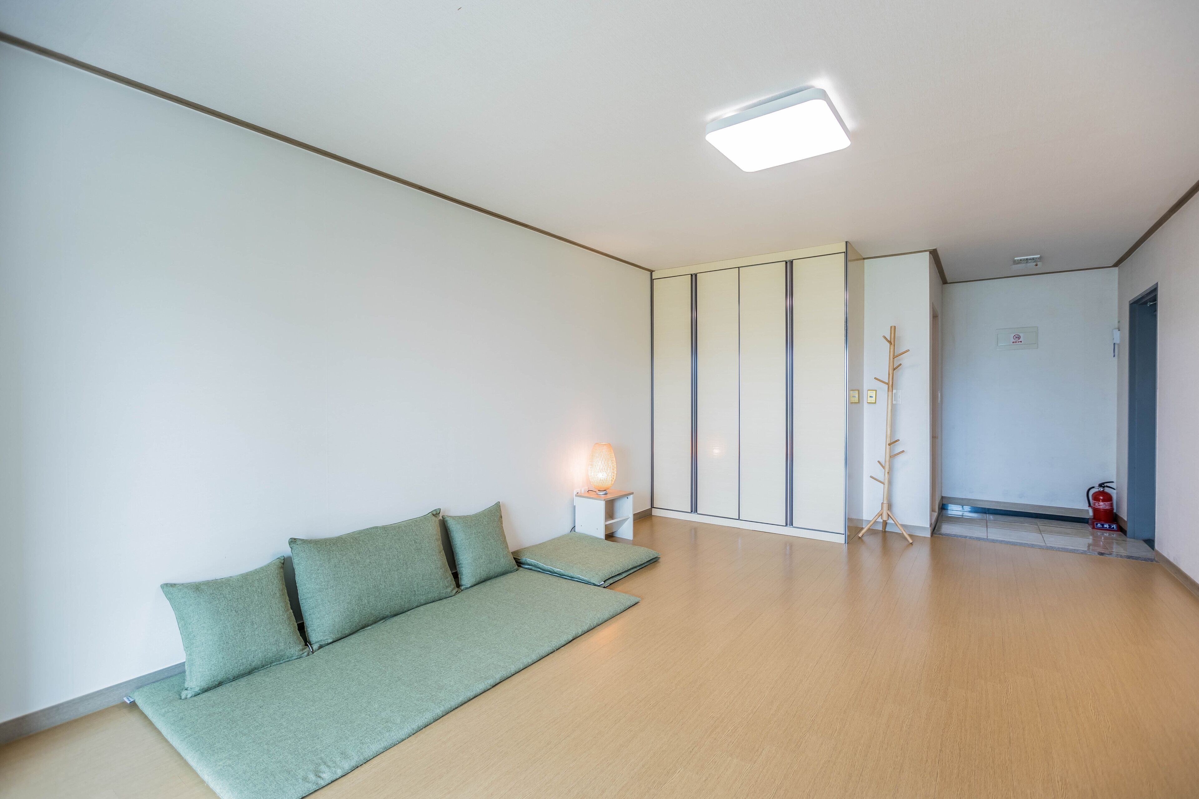 Una stanza minimalista con un divano verde, un tavolino con una lampada e un pavimento in legno.