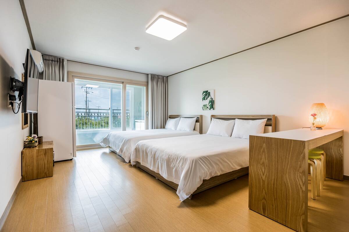 Habitación de hotel con dos camas, un escritorio de madera, un balcón con vistas y una lámpara en el techo.