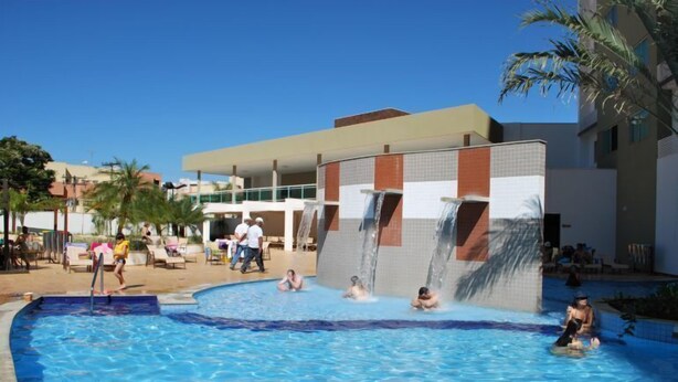 Una piscina con gente disfrutando, un edificio de fachada con azulejos y palmeras al fondo.