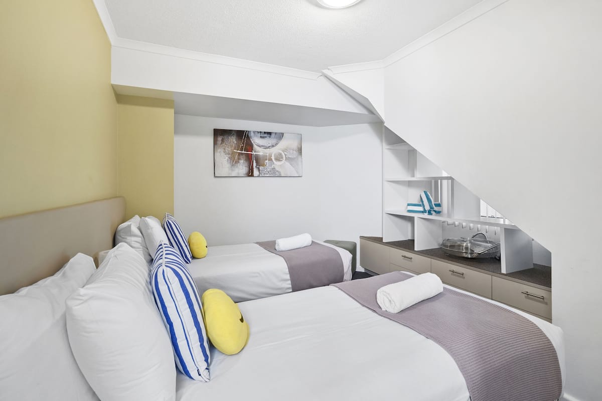 A hotel room with two beds, a desk with a computer, and a painting on the wall.