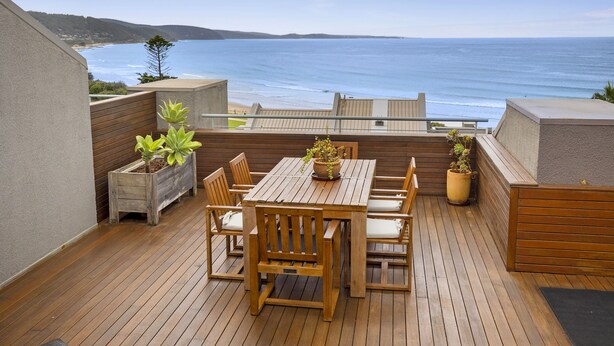 A wooden deck with a table and chairs, overlooking a beach. - Lorne Beachfront Accommodation (Lorne)