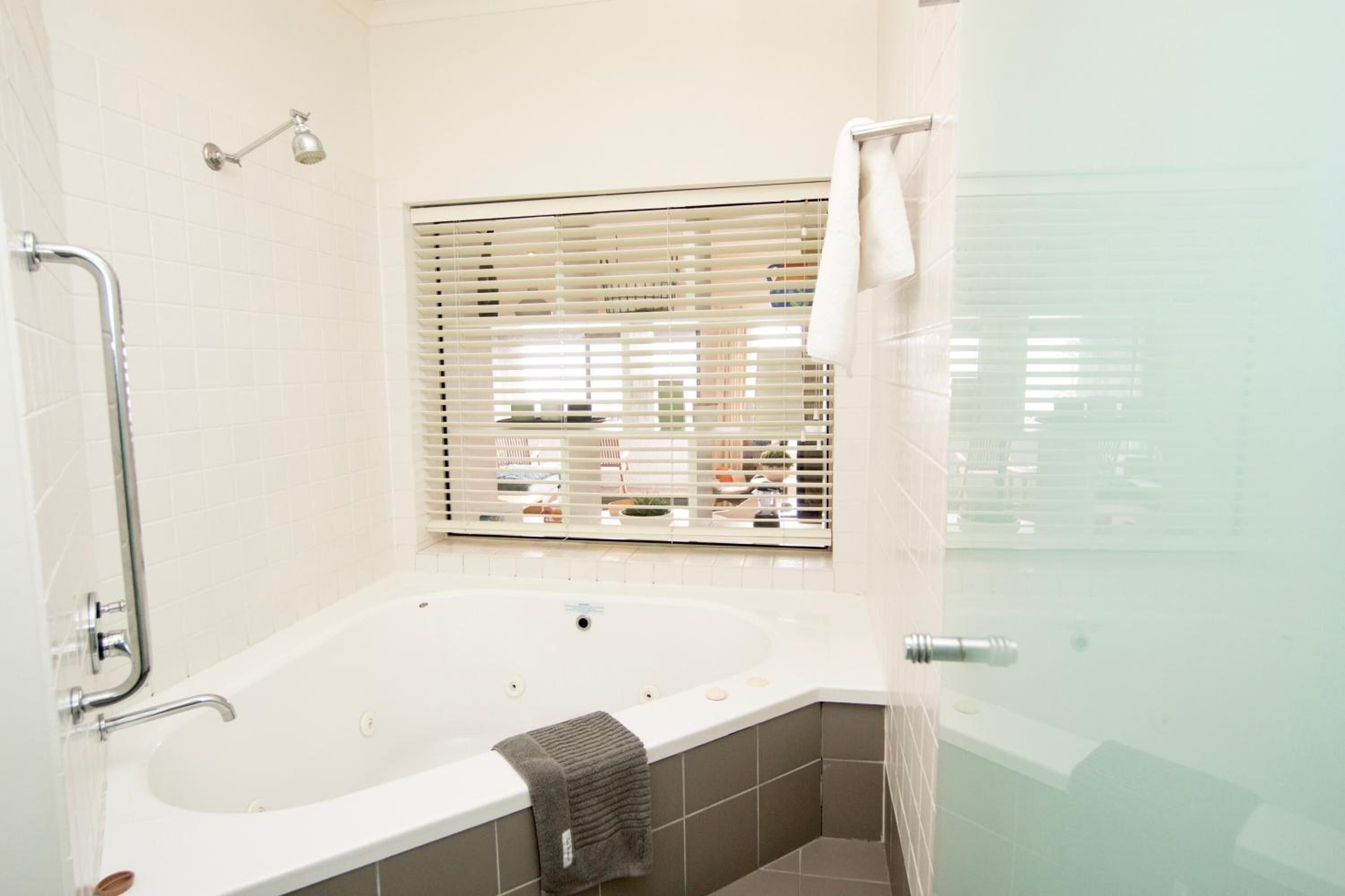 Une salle de bain moderne avec une baignoire sur pieds, une douche en verre et une fenêtre avec des stores.