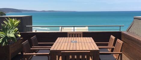 A wooden deck with a table and chairs, overlooking a coastal view.