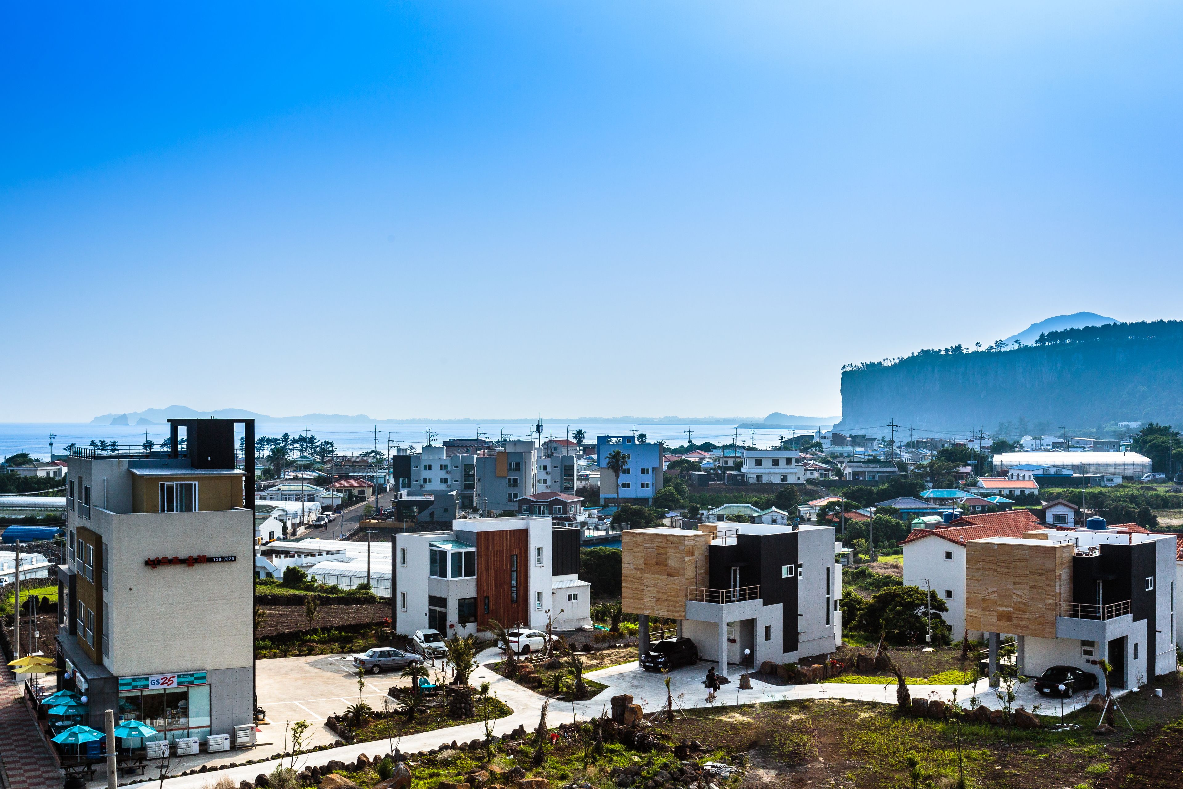 A modern residential area with contemporary houses, a visible commercial building, and a mountain in the background.