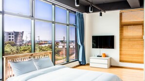 A modern bedroom with a large window, a bed, a bedside table, and a TV. - Amantov Pension (Seogwipo)