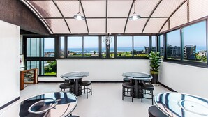 A modern, open-plan lounge area with large windows offering a view of the sea and cityscape. - Amantov Pension (Seogwipo)