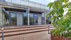 A building with a wooden deck, glass doors, and a metal railing. - Amantov Pension (Seogwipo)