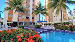 A hotel with a swimming pool, outdoor seating, and palm trees. -  Apartamento Jardins das Thermas - Achei Férias (com roupa de cama) (Caldas Novas)