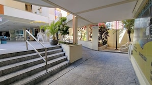 A hotel lobby with a staircase, indoor plants, and a seating area with chairs. -  Apartamento Jardins das Thermas - Achei Férias (com roupa de cama) (Caldas Novas)