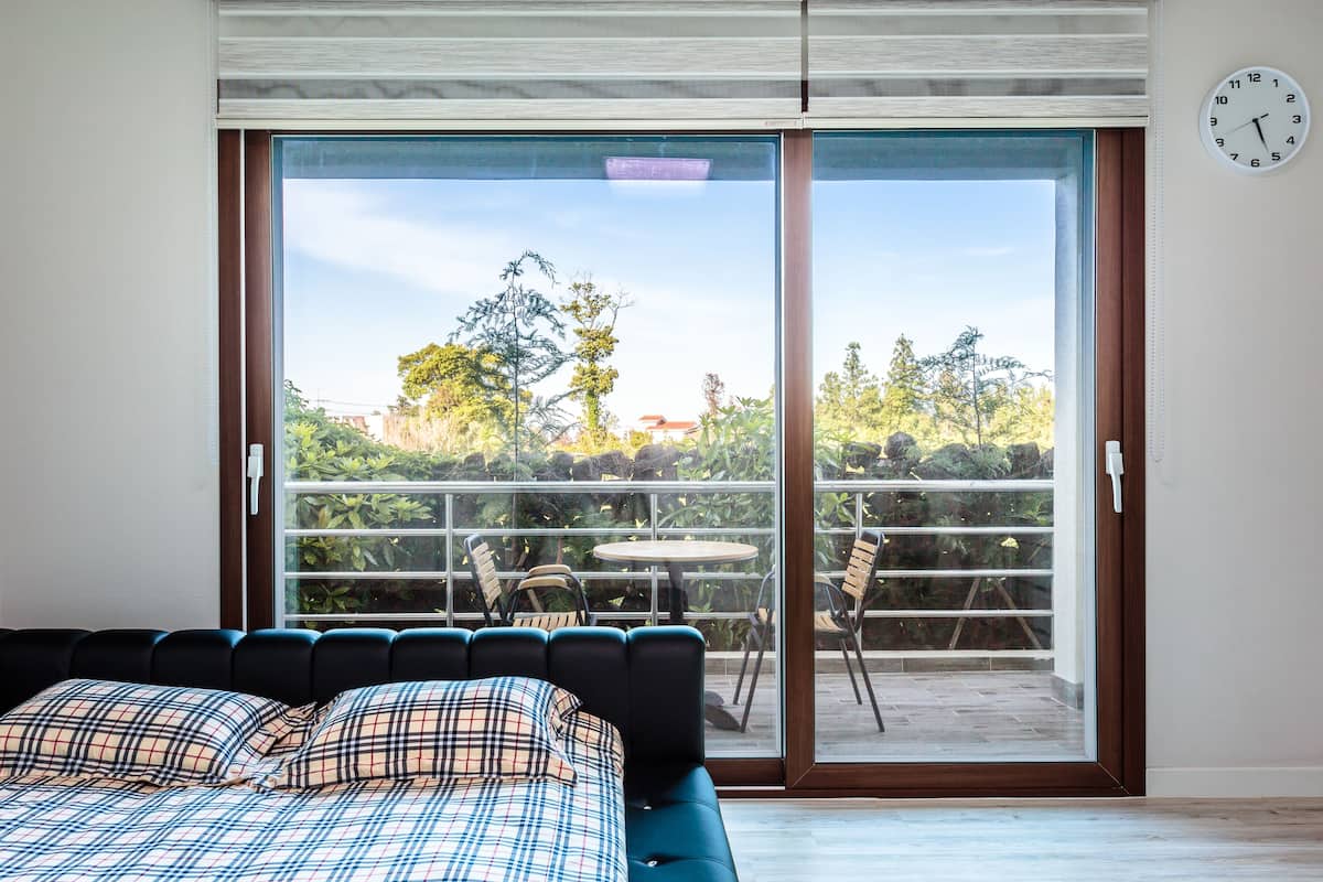 Quarto com cama, vista para uma varanda com cadeiras e mesa, e um relógio na parede.