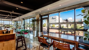 Un restaurante moderno con ventanas amplias, mesas de madera y sillas verdes.