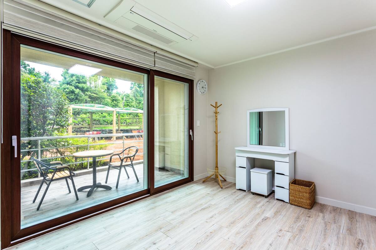 Quarto moderno com porta de vidro deslizante para um pátio externo, uma escrivaninha branca com espelho e um pequeno armário branco.